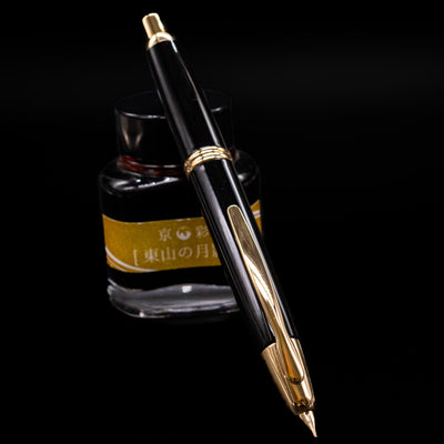 Pilot Vanishing Point Fountain Pen in black and gold resting on Kyo-no-oto ink bottle with gold label