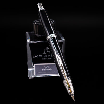 Pilot Vanishing Point Decimo Fountain Pen in Black and Rhodium resting diagonally on Jacques Herbin Gris de Houle ink bottle with nib exposed