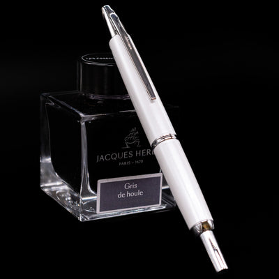 Side view of Pilot Vanishing Point Decimo Fountain Pen in White resting on Jacques Herbin Gris de Houle ink bottle
