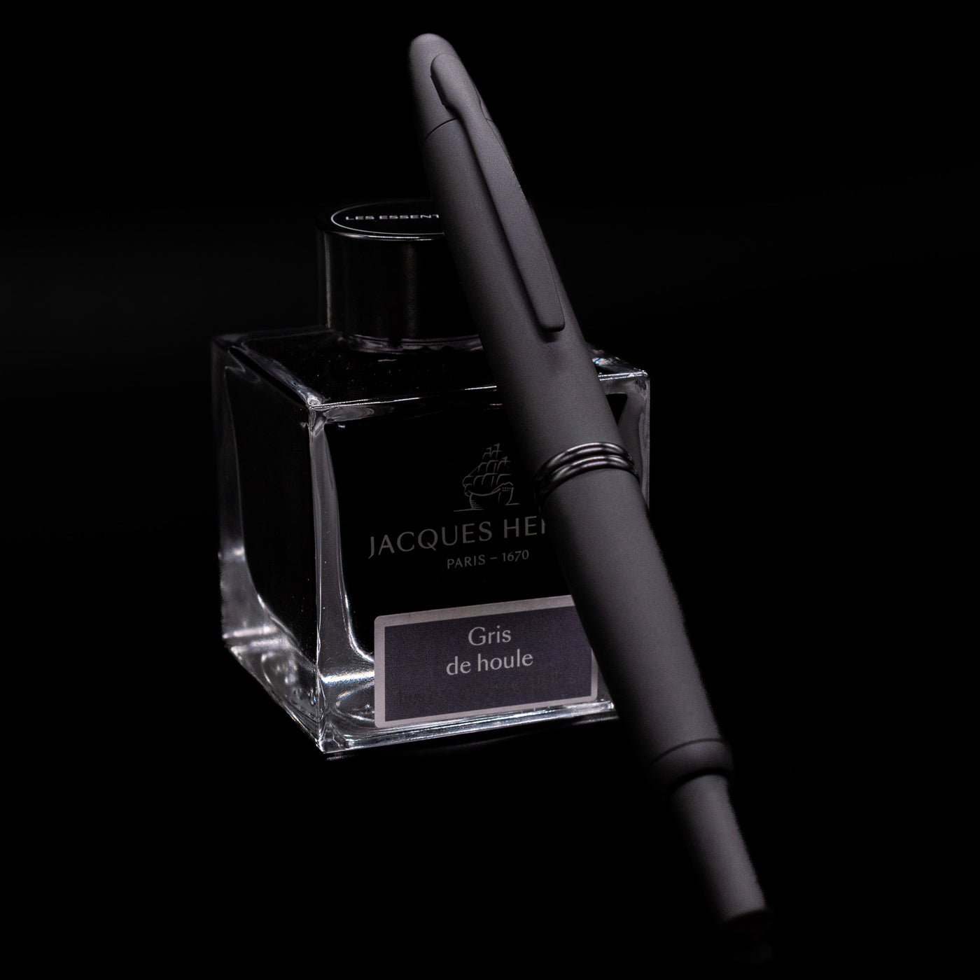 Angled view of Pilot Vanishing Point Fountain Pen in Black Matte leaning on Jacques Herbin ink bottle