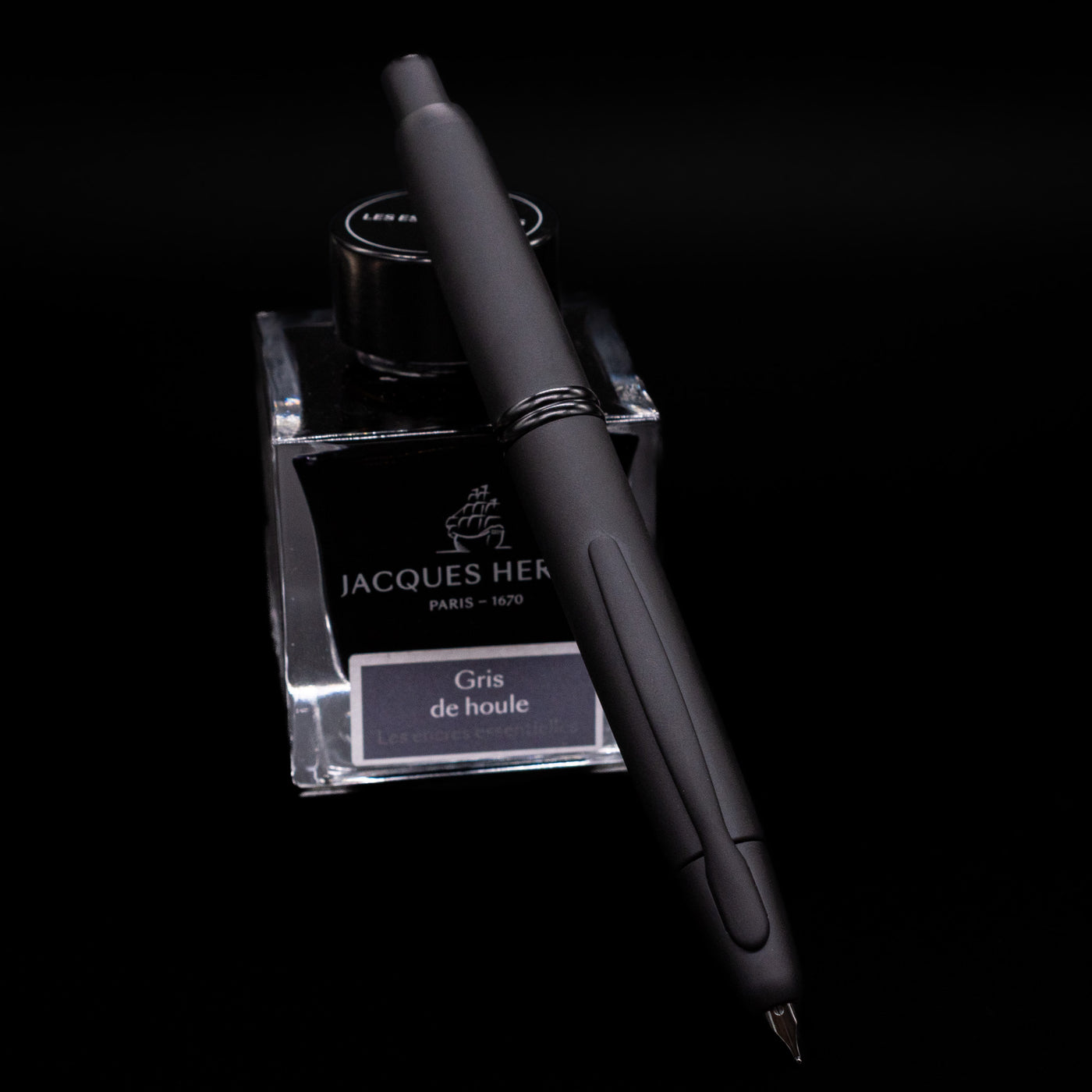 Pilot Vanishing Point Fountain Pen in Black Matte with nib extended, resting on Jacques Herbin Gris de Houle ink bottle
