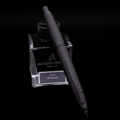 Pilot Vanishing Point Fountain Pen in Black Matte with nib extended, resting on Jacques Herbin Gris de Houle ink bottle