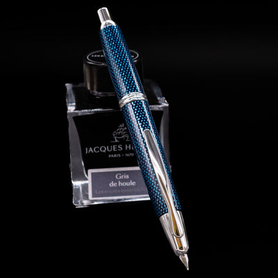 Angled view of Pilot Vanishing Point Fountain Pen Blue Carbonesque displayed on Jacques Herbin ink bottle