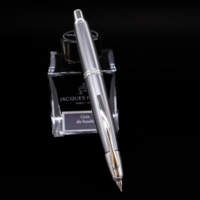 Pilot Vanishing Point Fountain Pen in Gun Metal with nib extended, displayed on Jacques Herbin Gris de Houle ink bottle