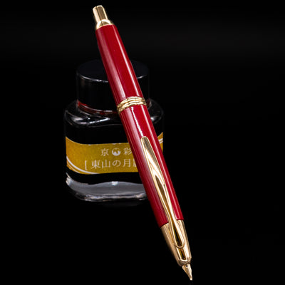 Pilot Vanishing Point Fountain Pen in Red with Gold accents standing upright in front of an ink bottle