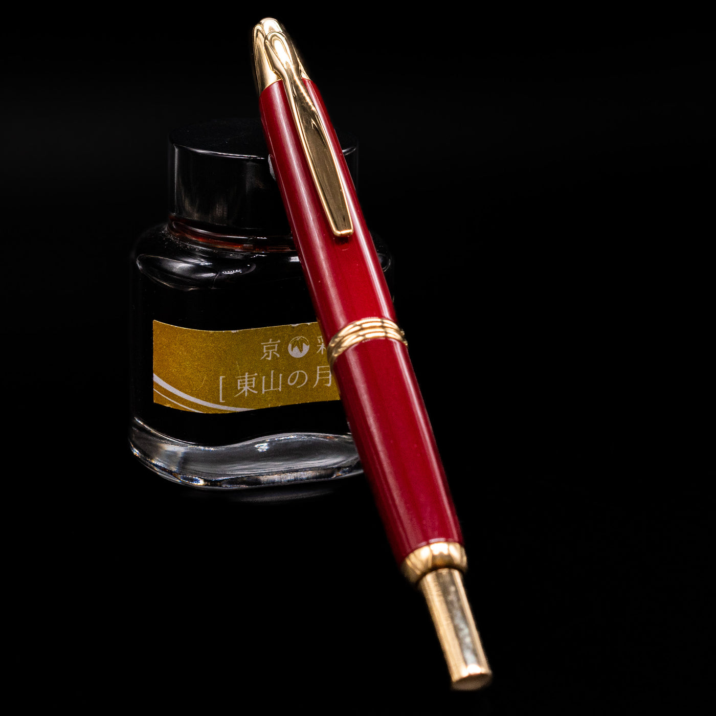 Pilot Vanishing Point Fountain Pen in Red with Gold Trim resting on yellow-labeled ink bottle, displayed on black background