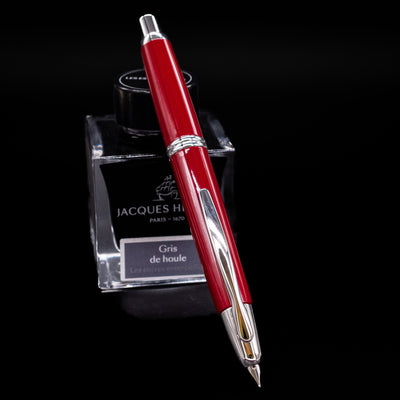 Pilot Vanishing Point Fountain Pen in Red with Rhodium Trim showing click mechanism, positioned on Jacques Herbin ink bottle