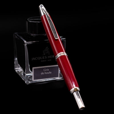 Pilot Vanishing Point Fountain Pen in Red with Rhodium Trim resting on Jacques Herbin Gris de Houle ink bottle