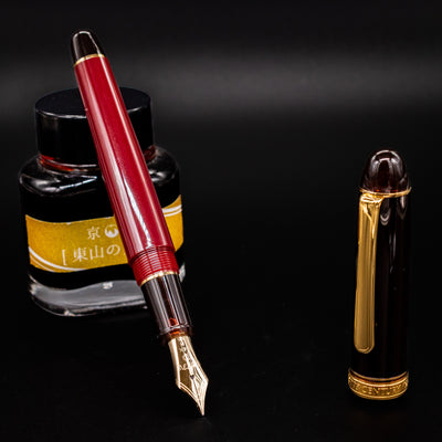 Platinum 3776 Century Fountain Pen in Coffee Jelly color shown uncapped with gold nib and ink bottle in background