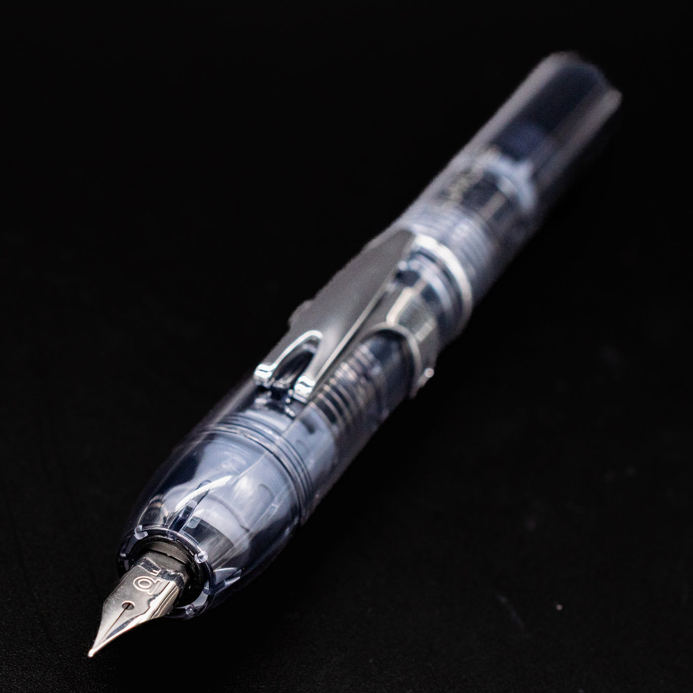 Angled close-up of the Platinum Curidas Fountain Pen - Graphite Smoke showing the transparent body and stainless steel nib.