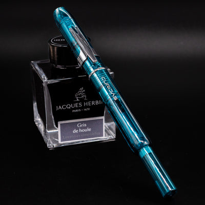 Platinum Curidas Fountain Pen - Urban Green shown capped and resting on Jacques Herbin Gris de Houle ink bottle.