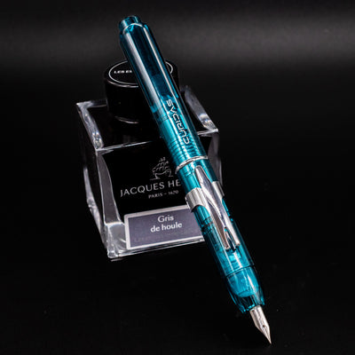 Platinum Curidas Fountain Pen - Urban Green shown open with nib exposed, resting on Jacques Herbin Gris de Houle ink bottle.