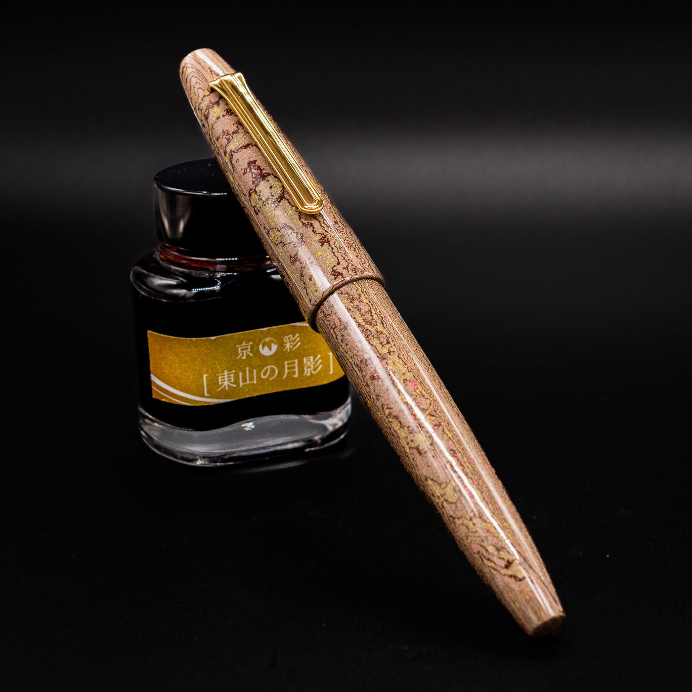 Sailor King of Pens Naginata Togi Syokei Fountain Pen shown capped with marbled ebonite body leaning against a bottle of ink on a dark background.