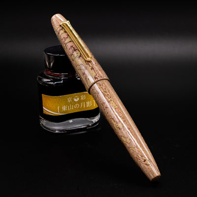 Sailor King of Pens Naginata Togi Syokei Fountain Pen shown capped with marbled ebonite body leaning against a bottle of ink on a dark background.