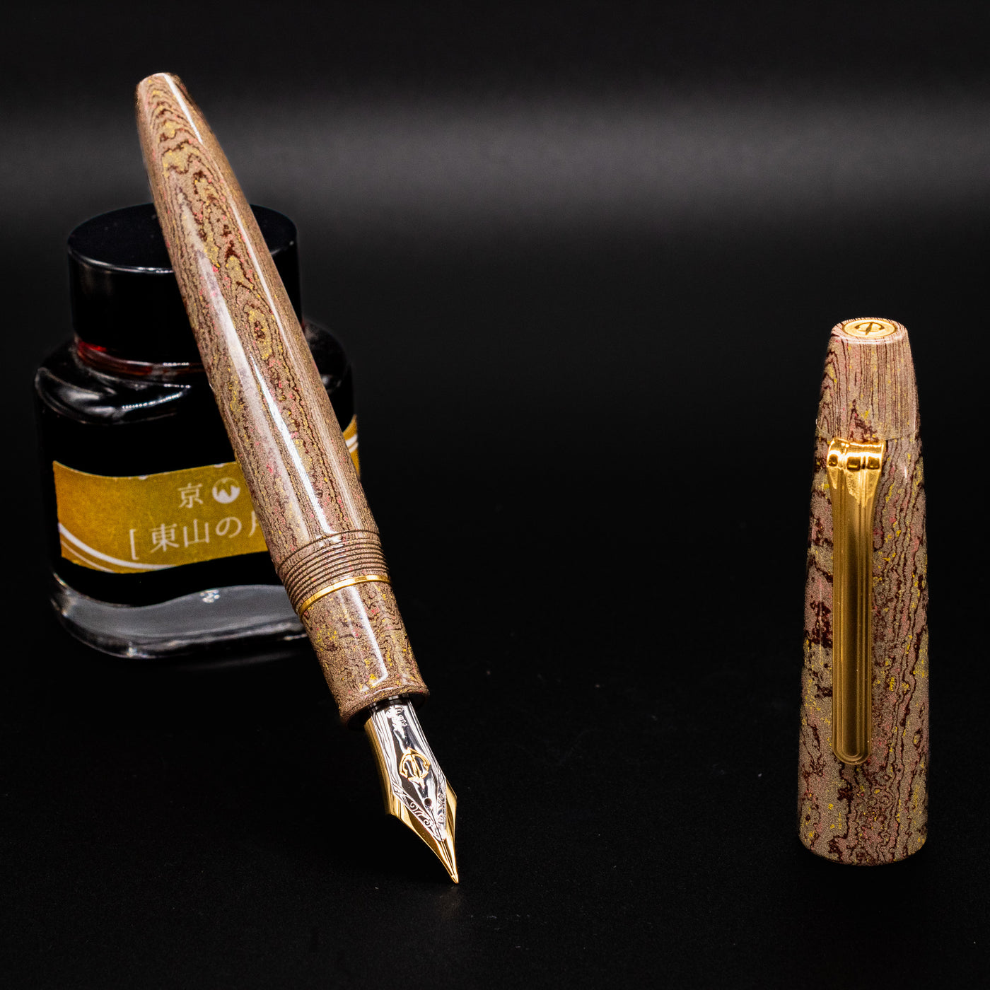 Sailor King of Pens Naginata Togi Syokei Ebonite Fountain Pen displayed uncapped with gold nib extended, matching marbled cap standing upright, and ink bottle in background on black surface.