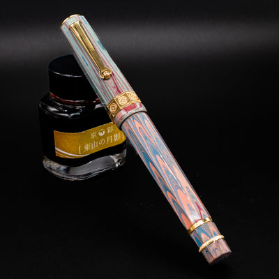 Santini Giant 8 Faceted Burano Fountain Pen shown capped in front of a gold-labeled ink bottle, highlighting its marbled pastel resin body and gold trim.