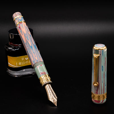 Santini Giant 8 Faceted Burano Fountain Pen shown open with gold nib extended, matching cap beside it, and ink bottle in the background on black surface.