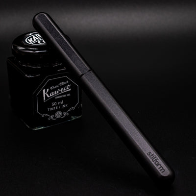 Stilform INK Fountain Pen Titanium DLC – capped and leaning on ink bottle