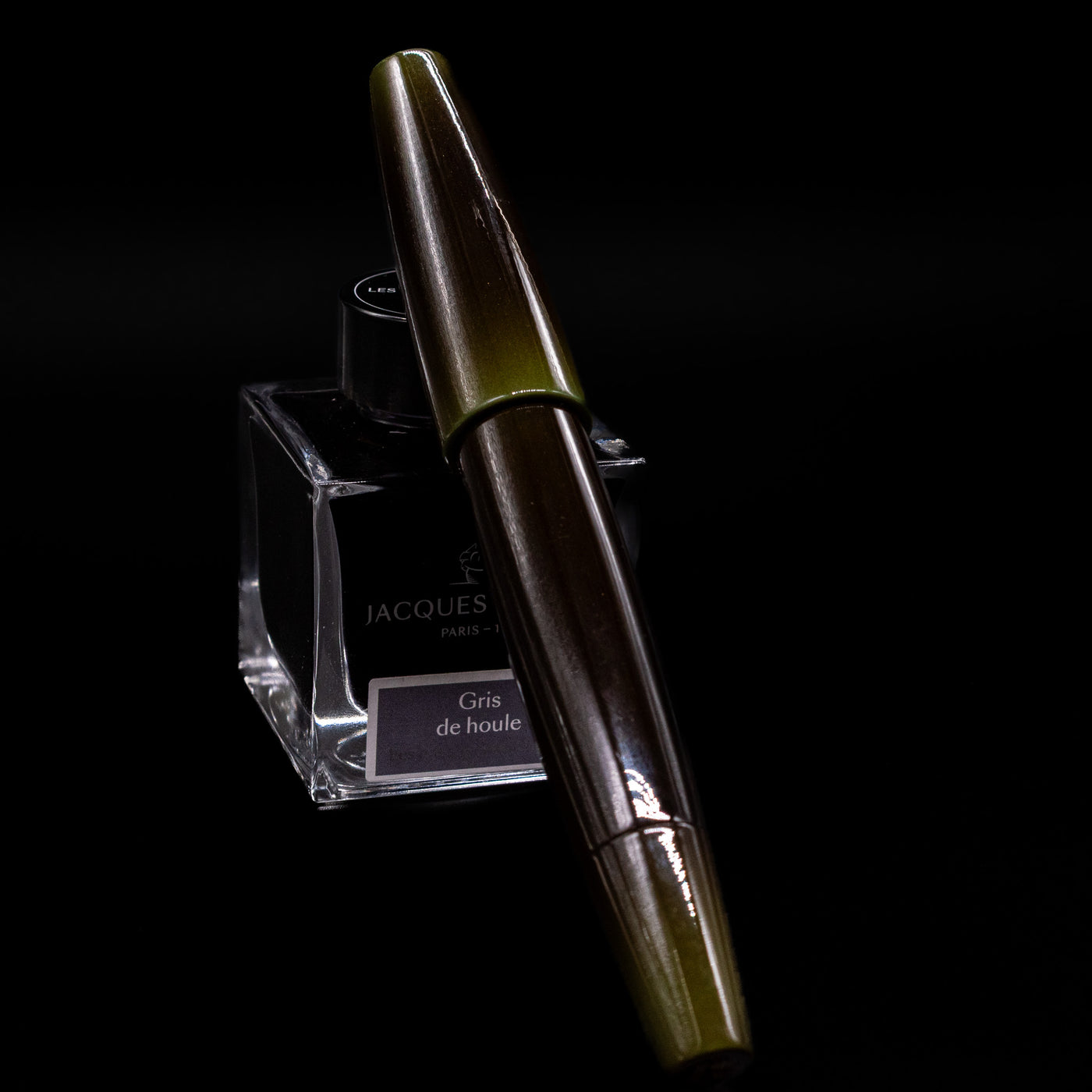 Capped Taccia Olive Green Gradiation Urushi Fountain Pen resting diagonally on Jacques Herbin ink bottle