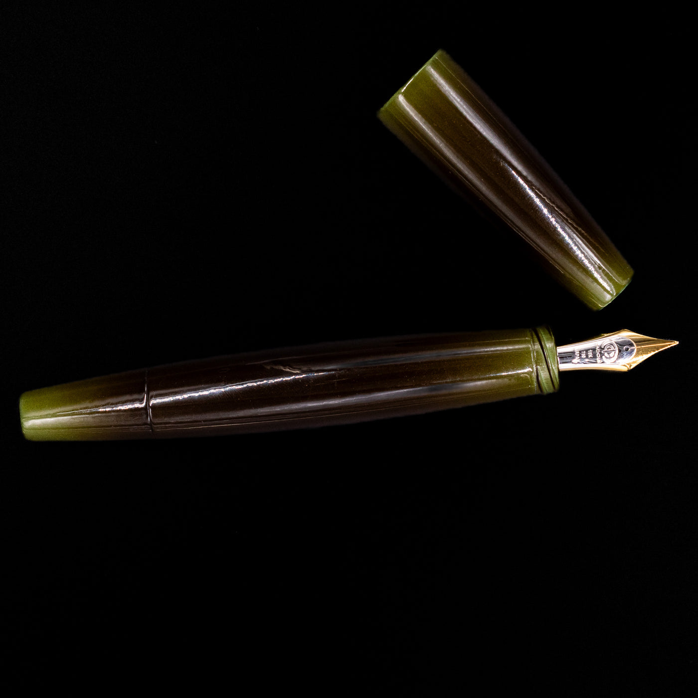 Flatlay of the Taccia Olive Green Gradiation Fountain Pen with cap and nib aligned on a black surface