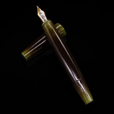 Top-down view of Taccia Olive Green Gradiation Urushi Fountain Pen with gold nib and cap placed horizontally