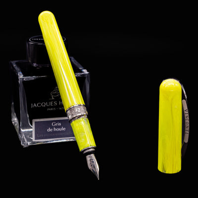 Visconti Breeze Fountain Pen in Lemon resting on Jacques Herbin Gris de Houle ink bottle with cap beside it
