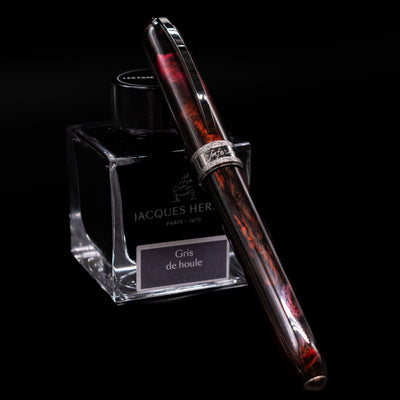 Full view of the Visconti Comedia Inferno Fountain Pen with cap on, displayed against Jacques Herbin ink