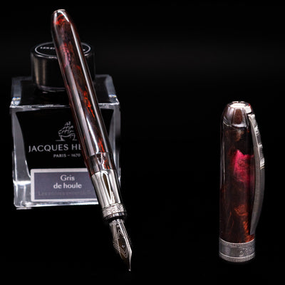 Visconti Comedia Fountain Pen - Inferno with nib exposed, resting on Jacques Herbin Gris de Houle ink bottle
