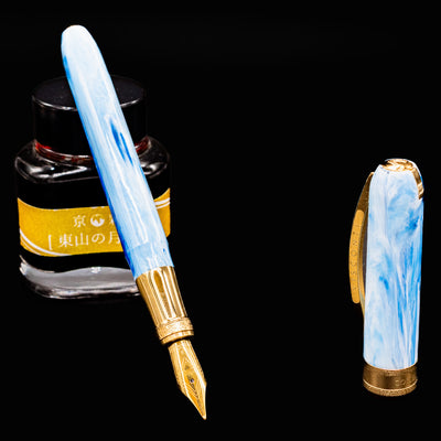 Visconti Comedia Paradiso fountain pen uncapped with gold nib beside yellow ink bottle on black background.