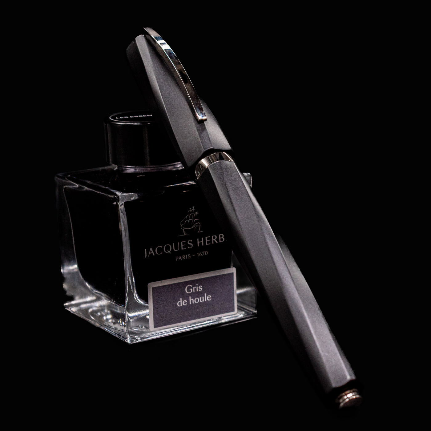 Visconti Divina Fountain Pen in Matte Black resting on Jacques Herbin Gris de Houle ink bottle on black background
