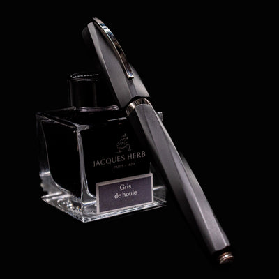 Visconti Divina Fountain Pen in Matte Black resting on Jacques Herbin Gris de Houle ink bottle on black background