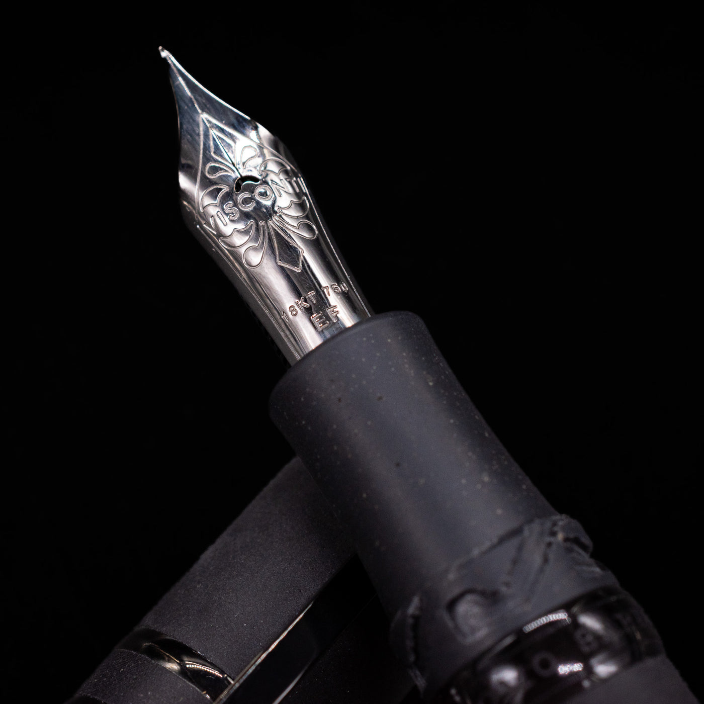 Close-up of a black Visconti Homo Sapiens fountain pen with an ornate 18k gold nib on a black background