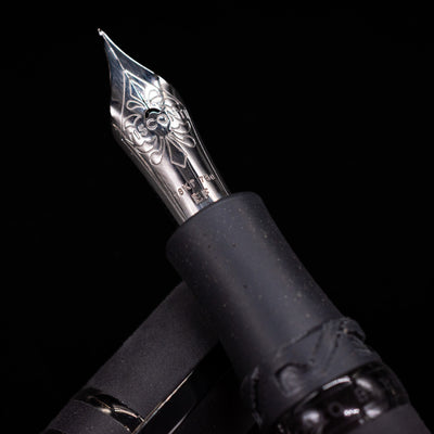 Close-up of a black Visconti Homo Sapiens fountain pen with an ornate 18k gold nib on a black background