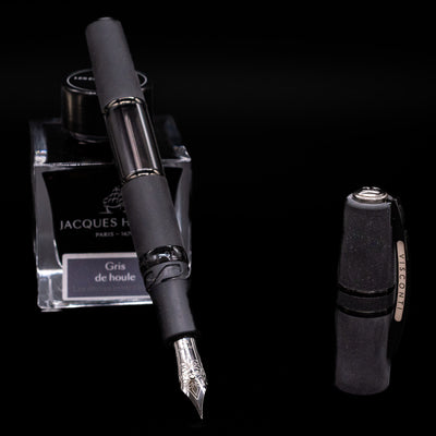 Black Visconti Homo Sapiens Dark Crystal fountain pen leaning on a Jacques Herbin ink bottle, based on a black background