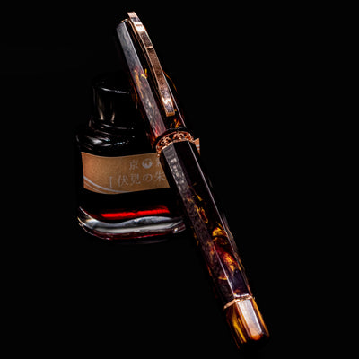 Visconti Medici Palazzo Pitti Fountain Pen resting on ink bottle with rose gold trim and fiery marbled resin barrel