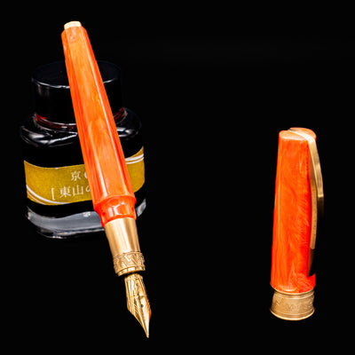 Visconti Mirage Mythos Fountain Pen Demeter with cap removed beside ink bottle showcasing gold nib and vibrant orange resin body
