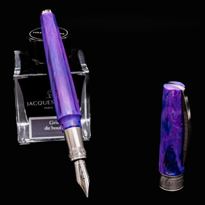 Visconti Mirage Mythos Fountain Pen in Persephone shown uncapped with nib facing forward, leaning on Jacques Herbin ink bottle
