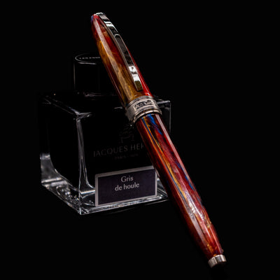 Visconti Van Gogh Red Vineyard Fountain Pen resting on Jacques Herbin ink bottle with a striking marbled red, orange, and blue resin body