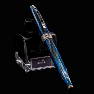 Visconti Van Gogh Starry Night Fountain Pen resting on Jacques Herbin Gris de Houle ink bottle, showcasing swirling blue and yellow resin.