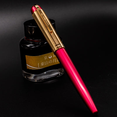 Capped Wahl Eversharp Skyline Fountain Pen in Red & Gold leaning against a bottle of ink for display.